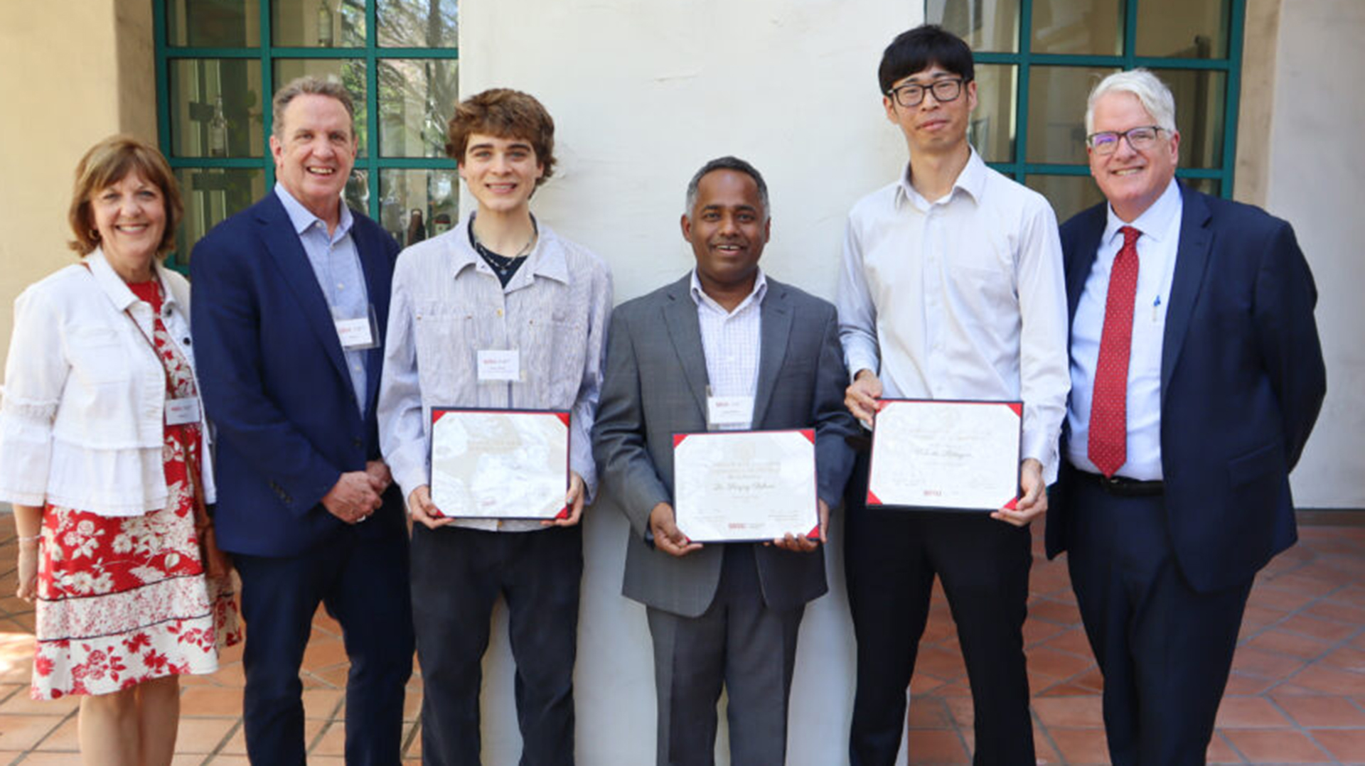 five people are standing in a row and smiling at the camera in which three people in the middle holding the 2025 excellence award.