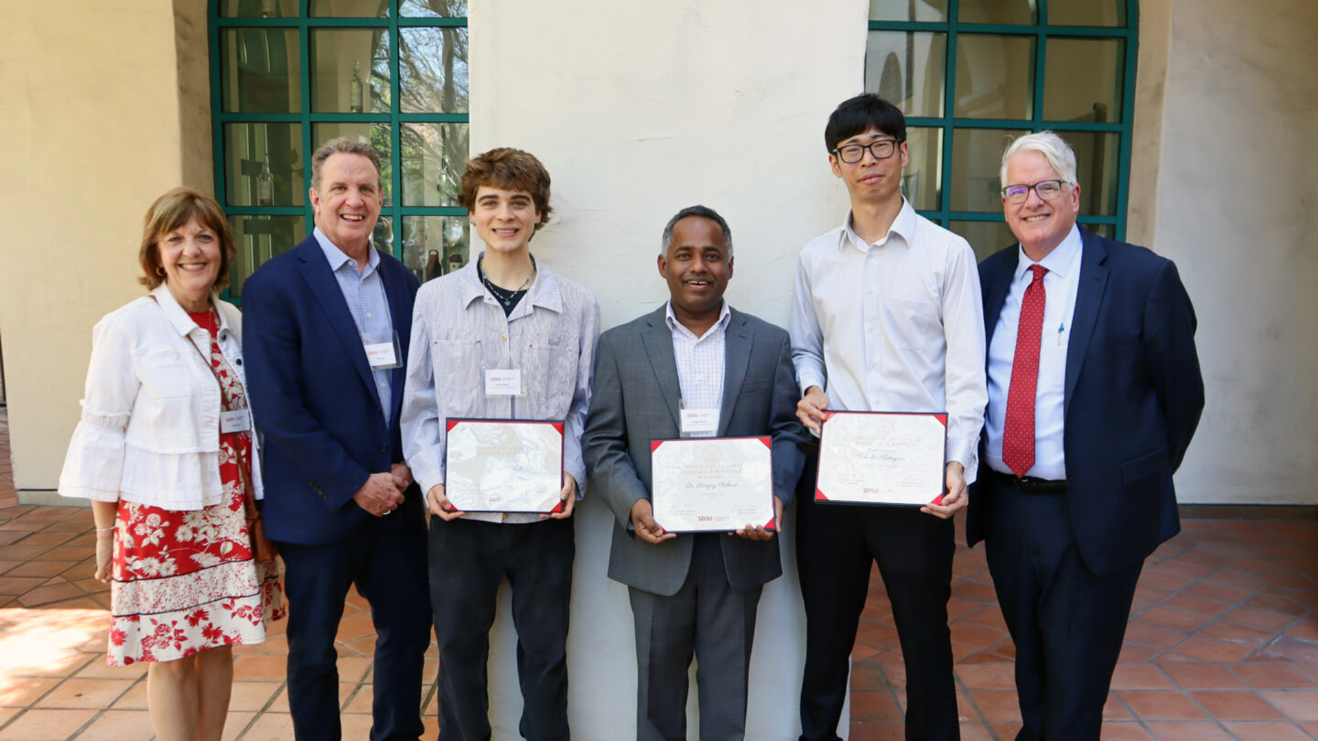 six people are standing in a row and smiling at the camera in which three people in the middle are holding the excellence award in their hand