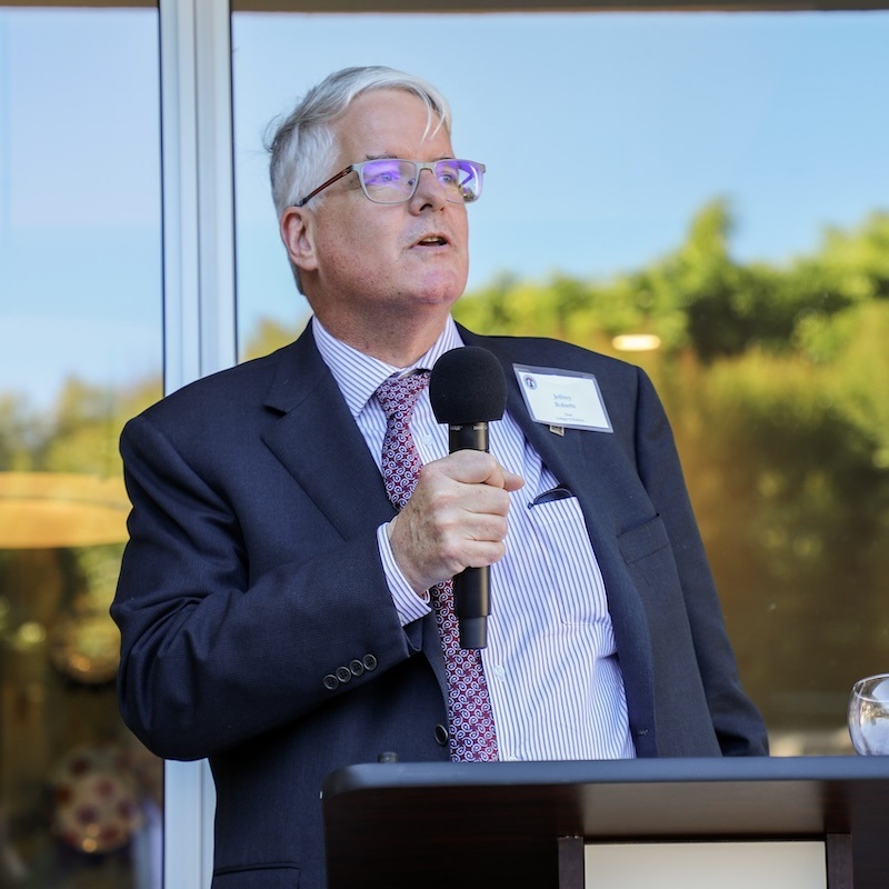Closeup of Jeff Roberts at podium, holding microphone.