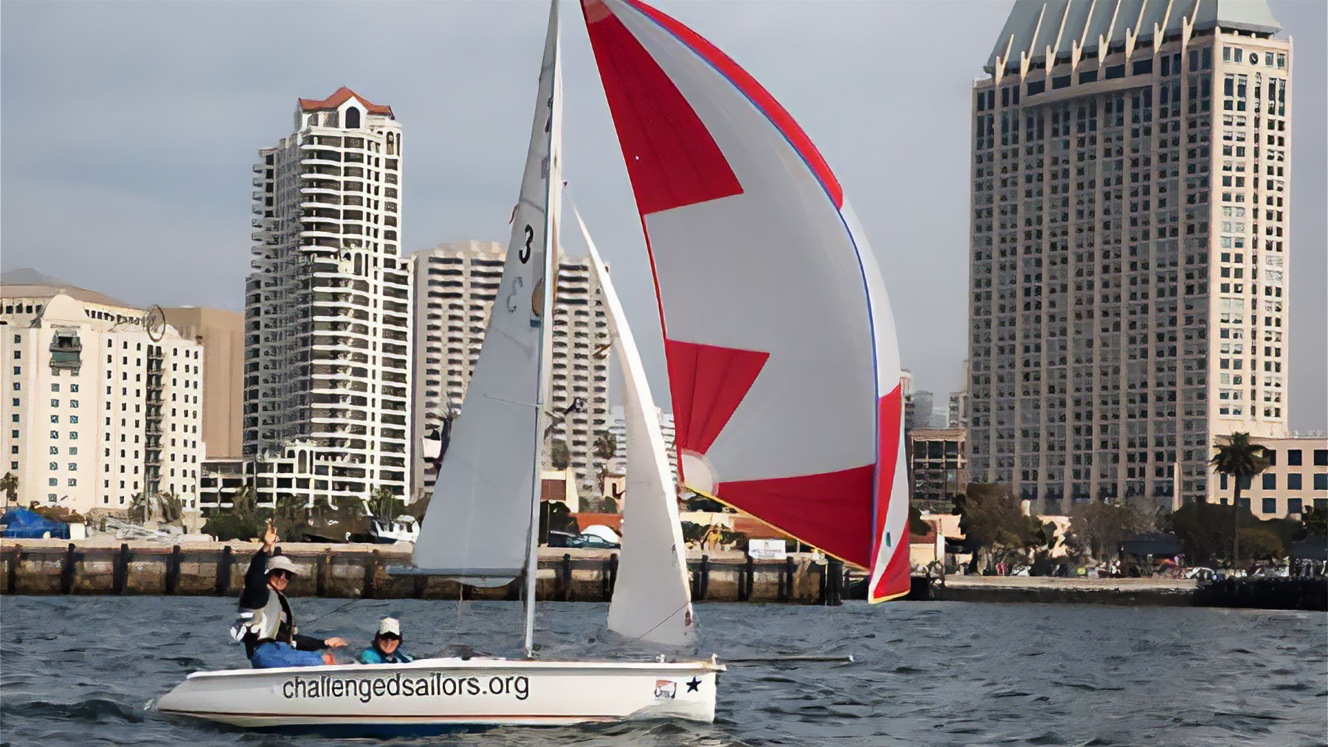 Sail boat in San Diego Harbor with buildings behind.