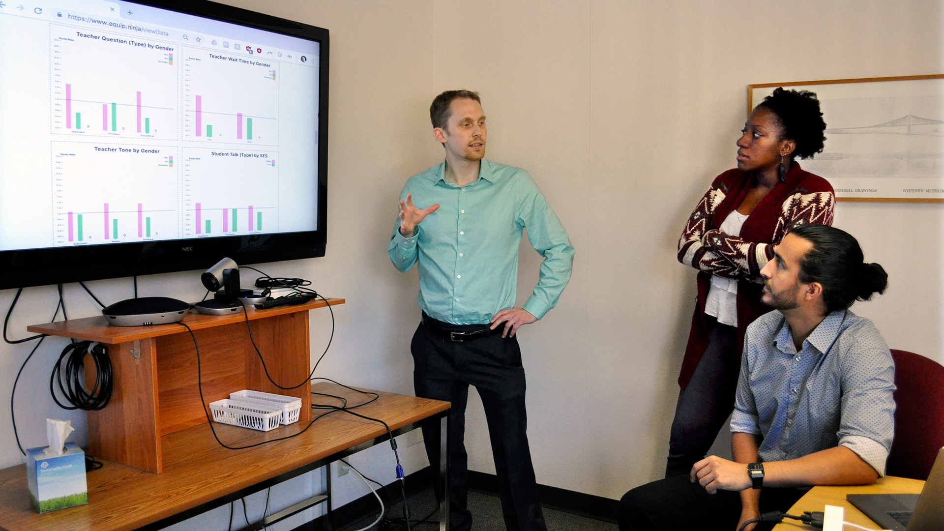 Daniel Reinholz demonstrates an app he developed to evaluate classroom equity to his students Amelia Stone and Antonio Martinez. 