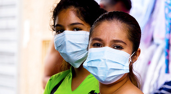 close-up of latinas wearing thin light blue masks over mouth and nose