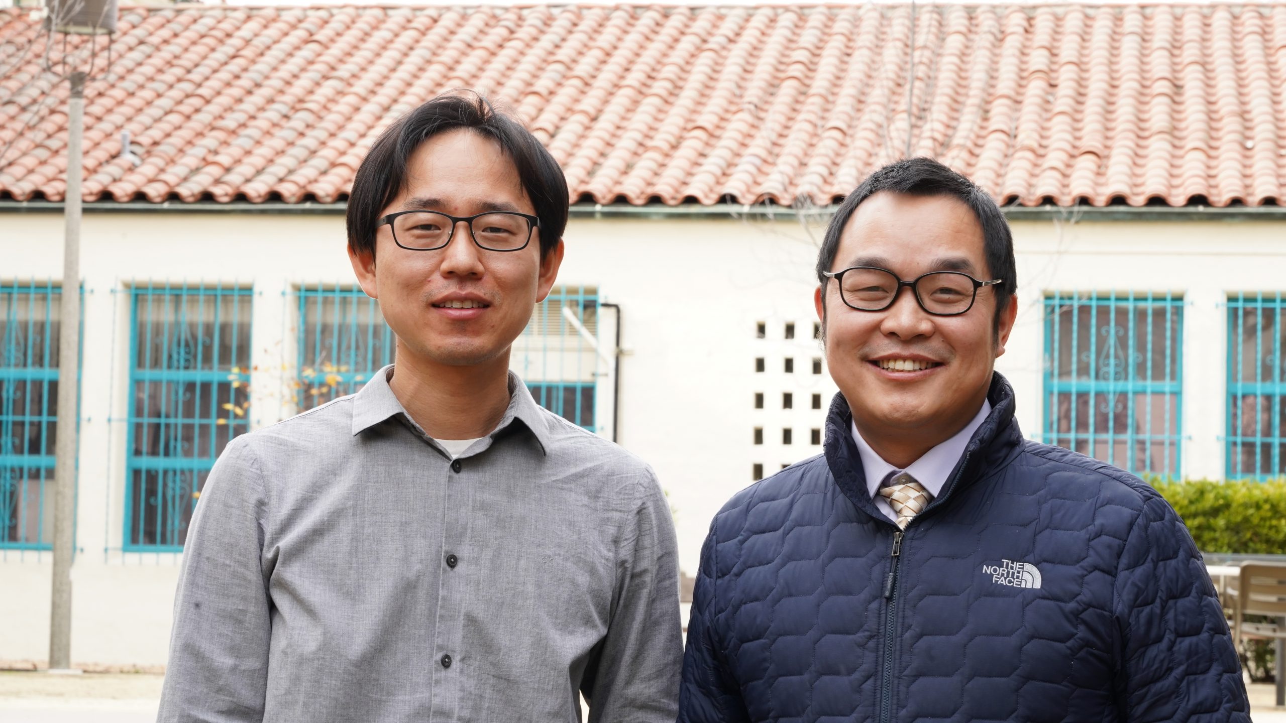 Youngkwang Lee (left) and Yong Yan smile while standing in front of a Spanish style building with teal trim on the windows.