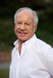 A man in a white shirt smiles outside