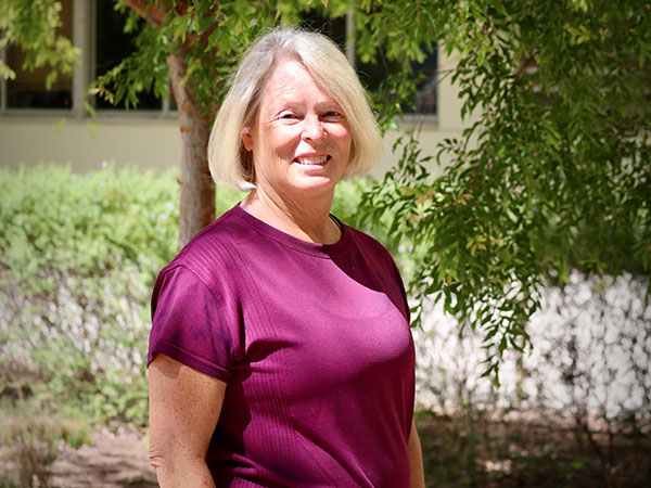 Woman with chin-length blonde hair wearing a magenta shirt smiles outside with trees in background