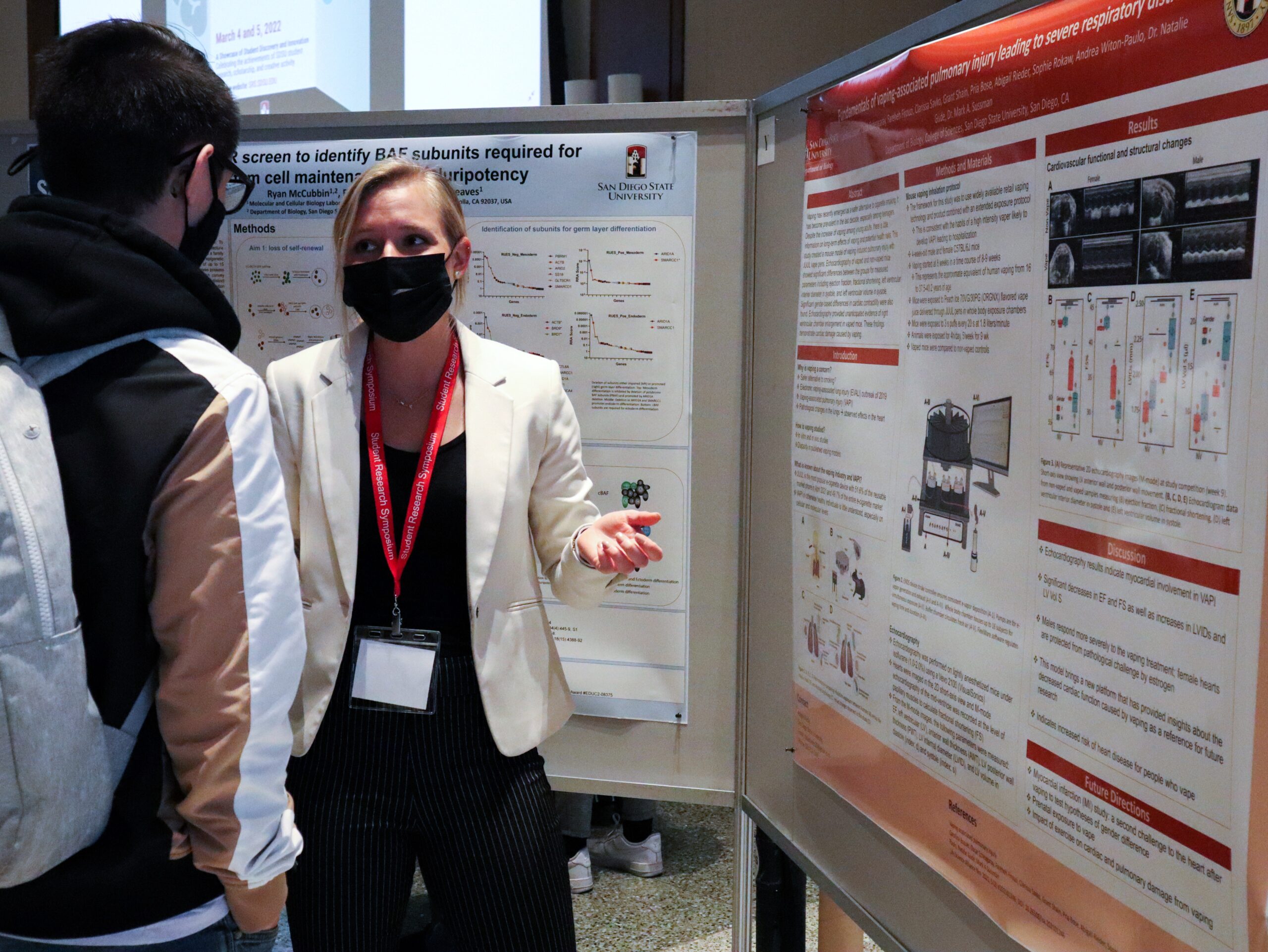 Blonde woman wearing white blazer discussers poster with another SDSU community member.