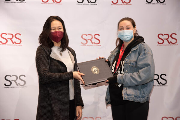 A faculty member awards a student an award; they are both wearing masks.