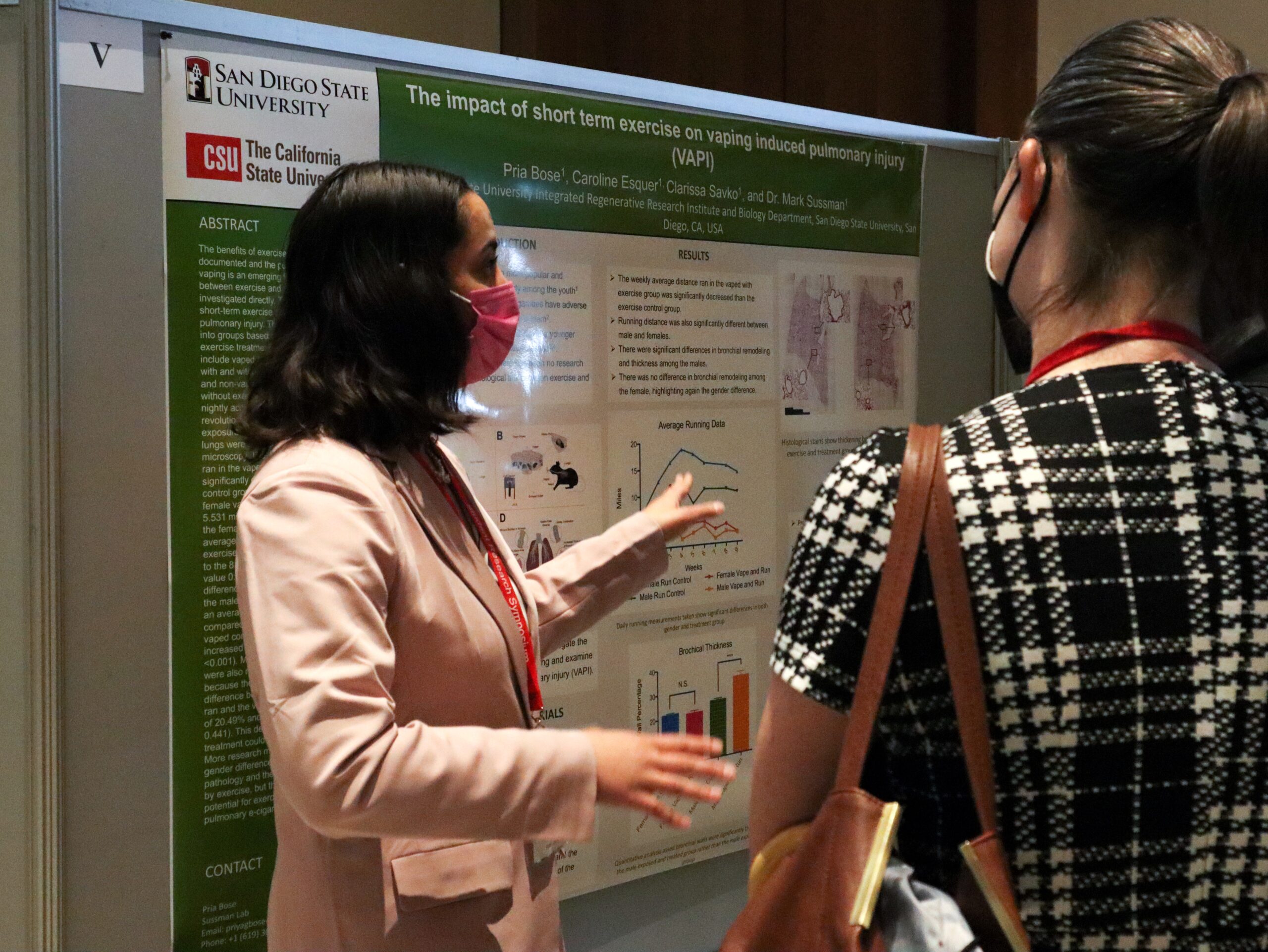 Young woman in pink blazer gestures as she explains her research poster