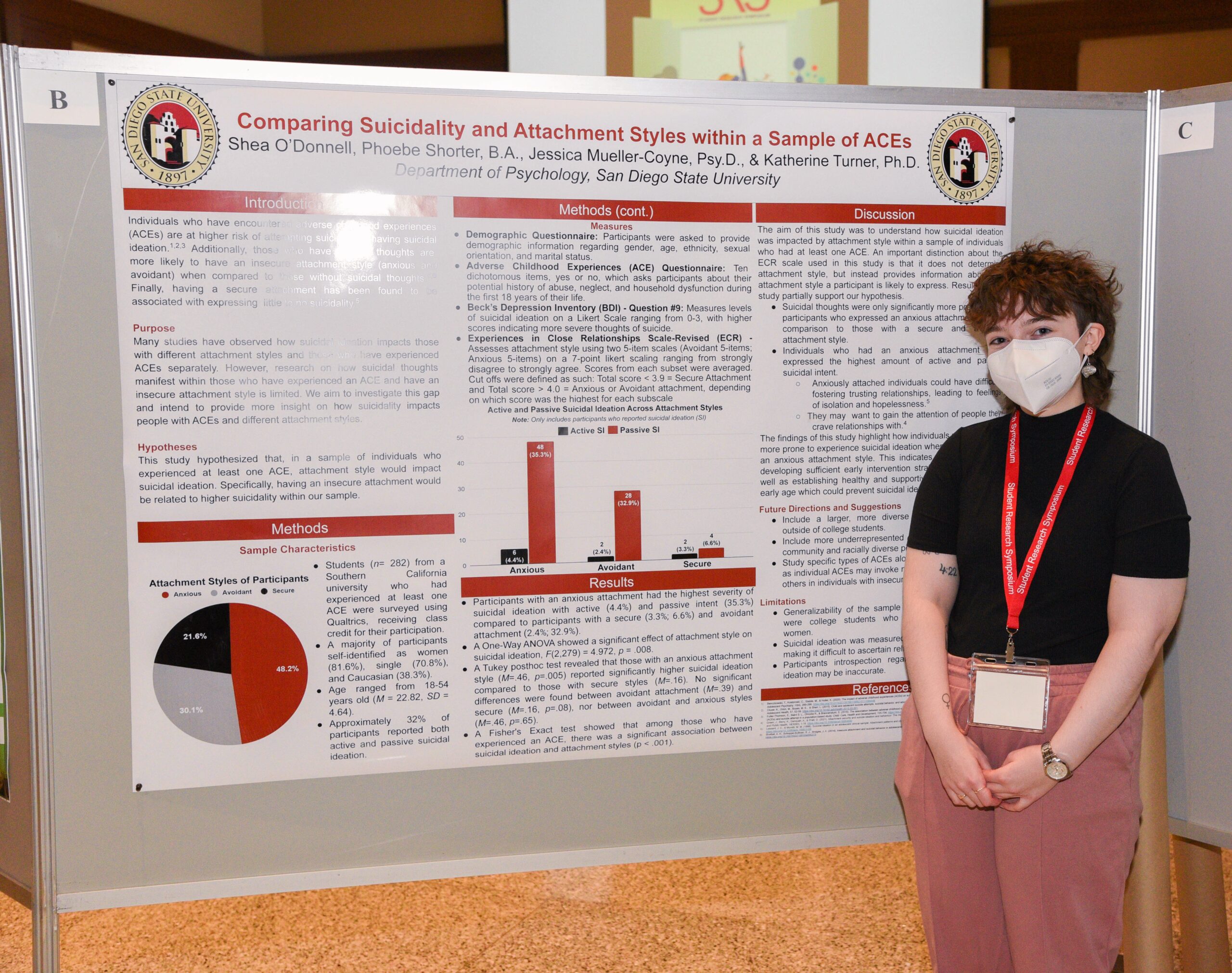 A person wearing a black top and reddish pants stands in front of a research poster