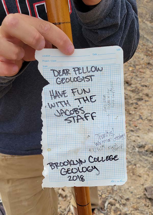 A student's hand holds up a note that reads 'dear fellow geologist, have fun with the Jacob's staff' with messages from multiple colleges. Photo credit: Rob Hawk