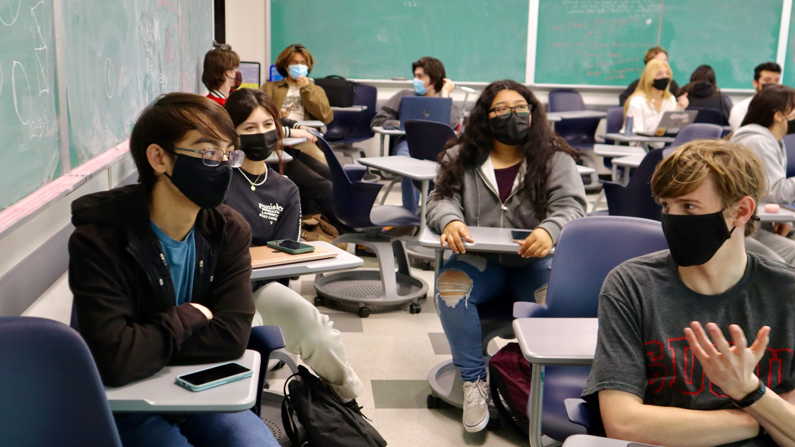 Students in CS 100 class discuss answers to interactive clicker questions in small groups while sitting in chairs. Their phones are on their desks and they are wearing masks.