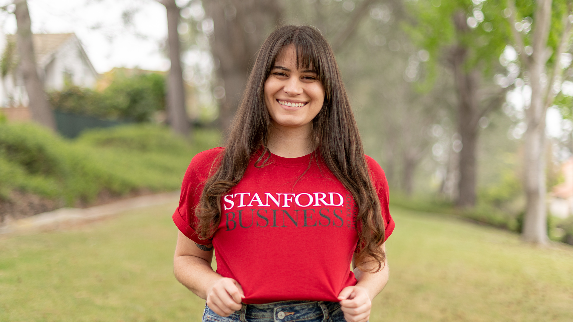 Woman with long brown hair shows off her red Stanford Business school t-shirt outside
