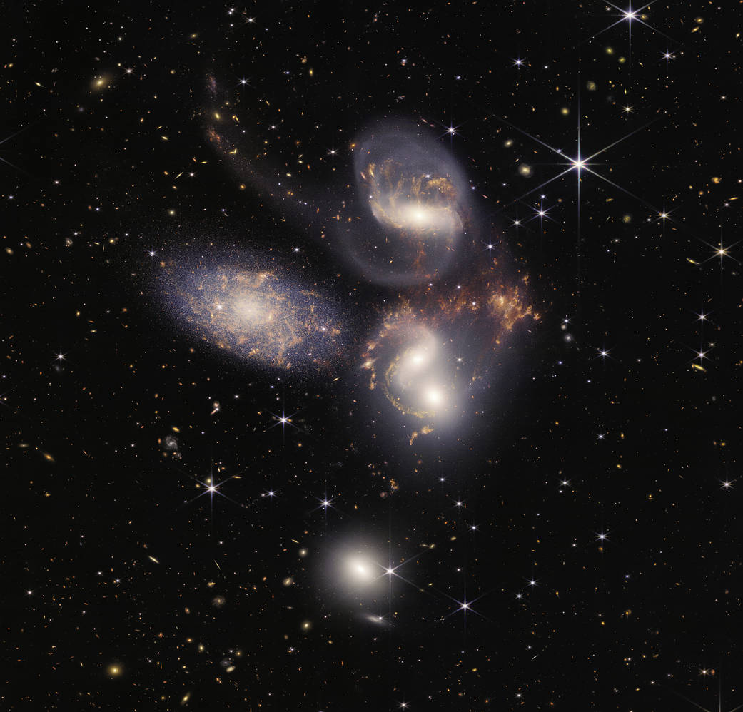 Five pinkish-white galaxies swirling around with some reddish-orange matter between them.