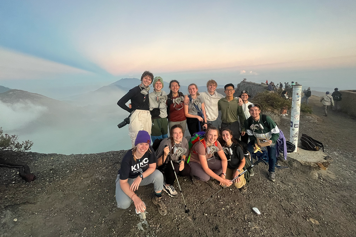 The whole group squats and smiles for a picture atop the sulfuric volcano at sunrise