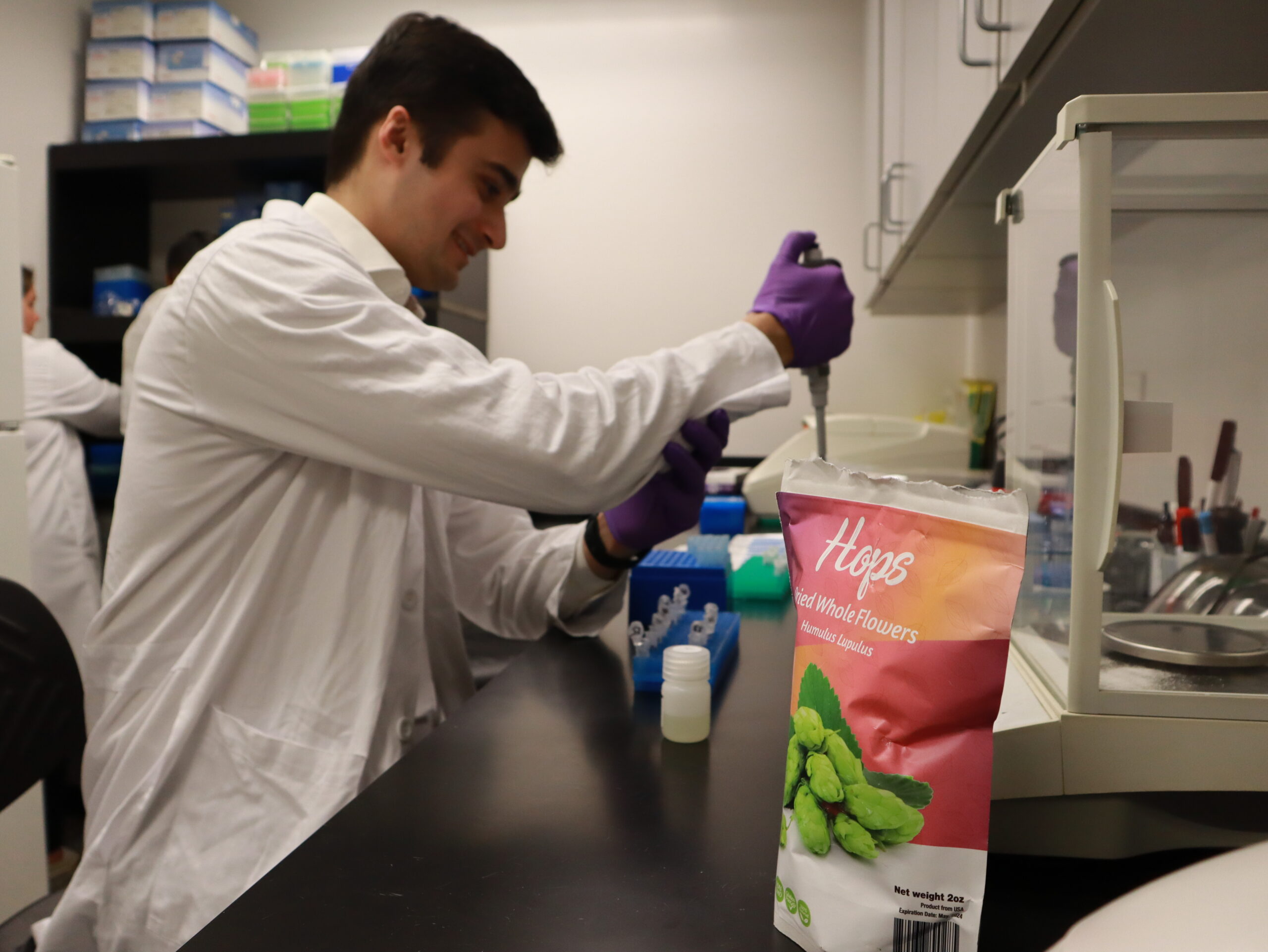 Ali Shah pipettes hops samples; a bag of hops is visible in the foreground