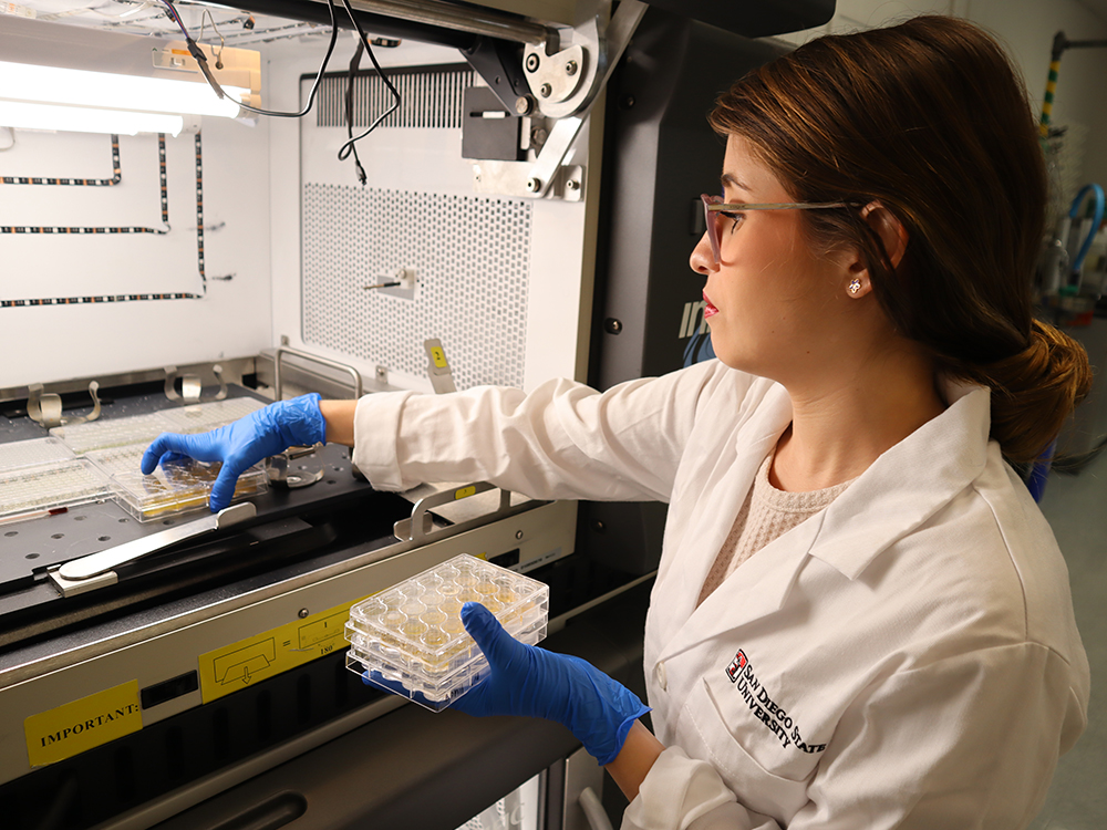 Gabriela Canto-Encalada in a lab coat places algae samples inside an incubator shaker.