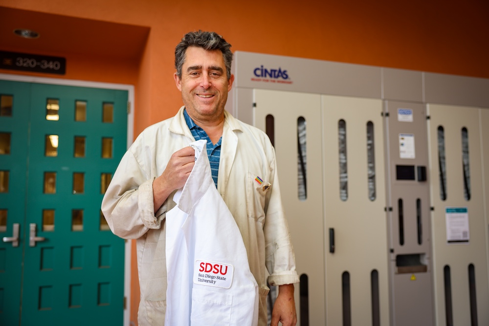 Man standing in white lab coat in front of machine