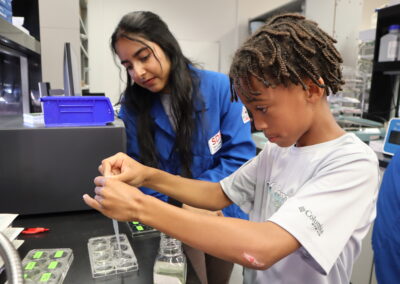 Undergraduate student Shaila Prasad assists a local fifth grade student in measuring and pipetting samples into wells