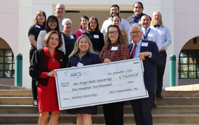 ARCS members presenting large check to President de la Torre, Dean Roberts, with 11 others posing behind on steps.